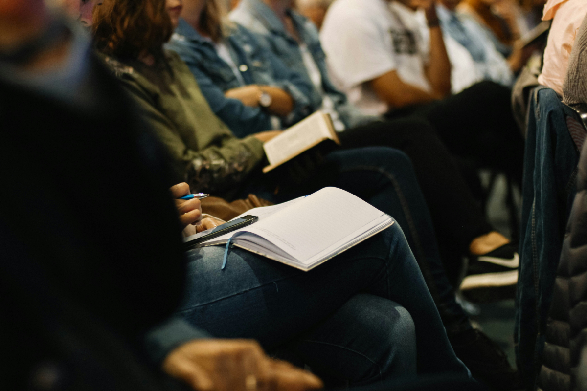 People sitting in a row with books in their laps and legs crossed, listening