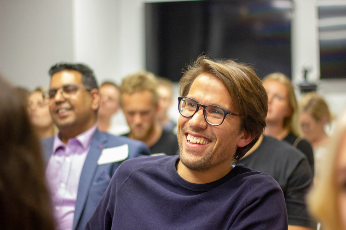 A man with glasses laughing with people behind him who are smiling